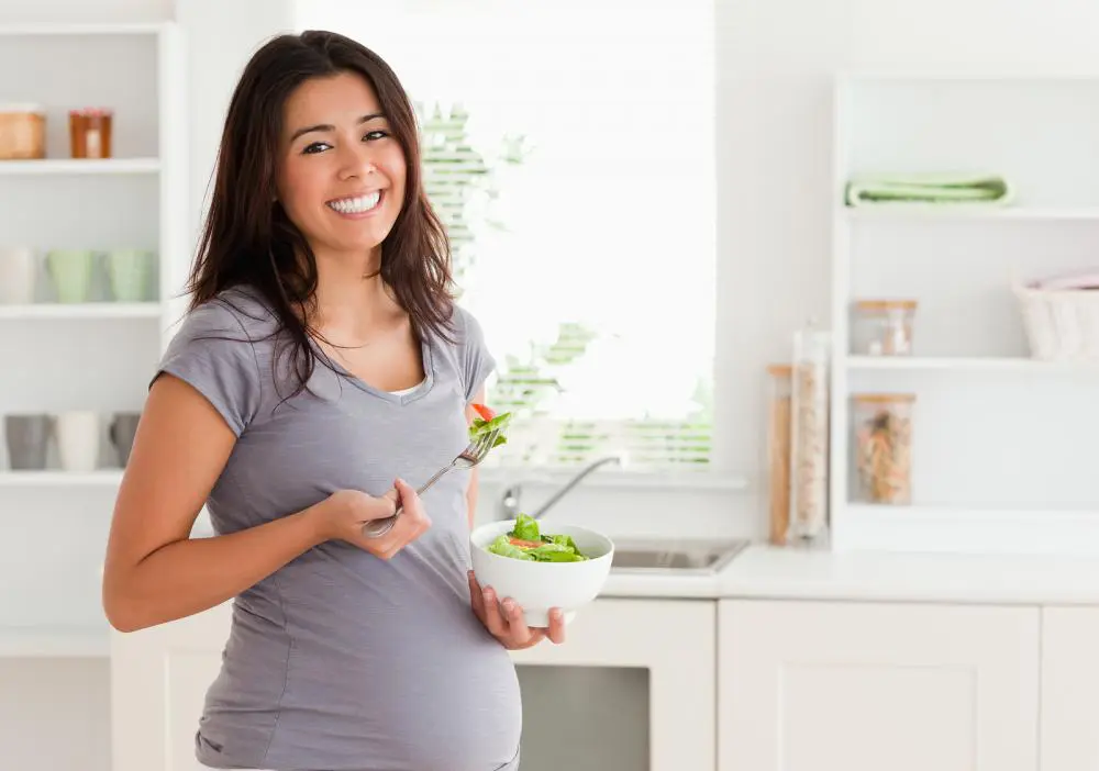pregnant woman with a salad in her hand and happy knowing that she can receive chiropractic care throughout her pregnancy in columbus with Dr. Hinze