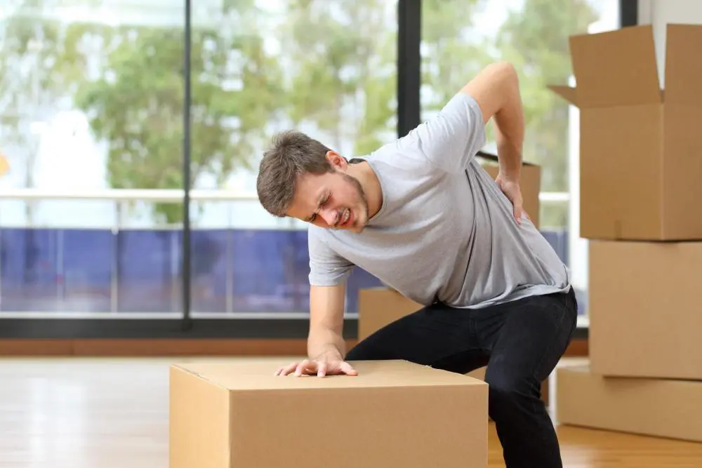 Man experiencing back pain from lifting boxes improperly.