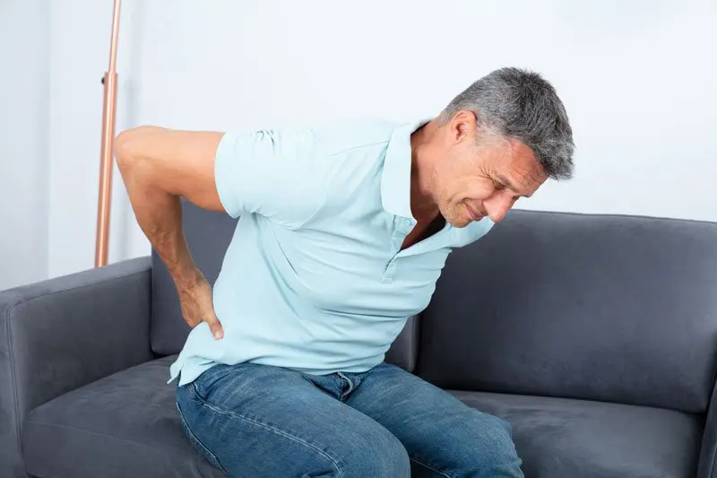 Senior man in pain sitting while holding his back due to pinched nerve.